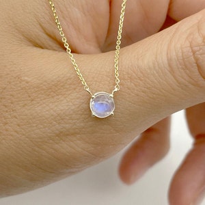 May include: A delicate gold chain necklace with a small, round moonstone pendant.