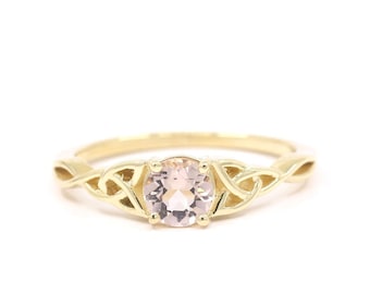 May include: A gold ring with a delicate Celtic knot design and a pale pink gemstone in the center.