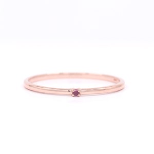 Peut inclure: Une délicate bague en or rose avec une seule petite pierre précieuse rouge rubis sertie au centre.