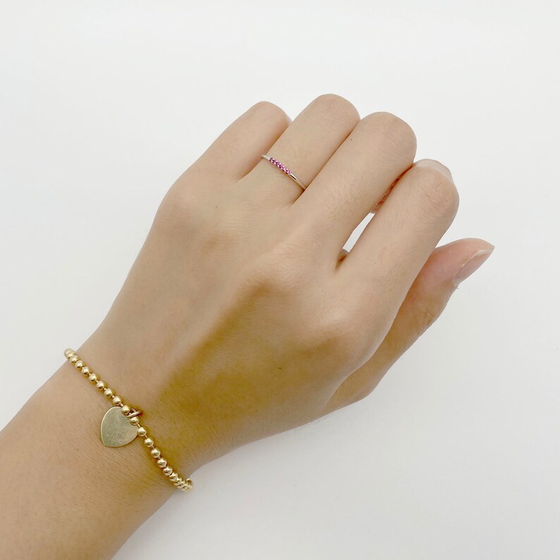 Puede incluir: Un brazalete de oro con un dije de coraz&oacute;n y un anillo delgado de oro con piedras rosas.