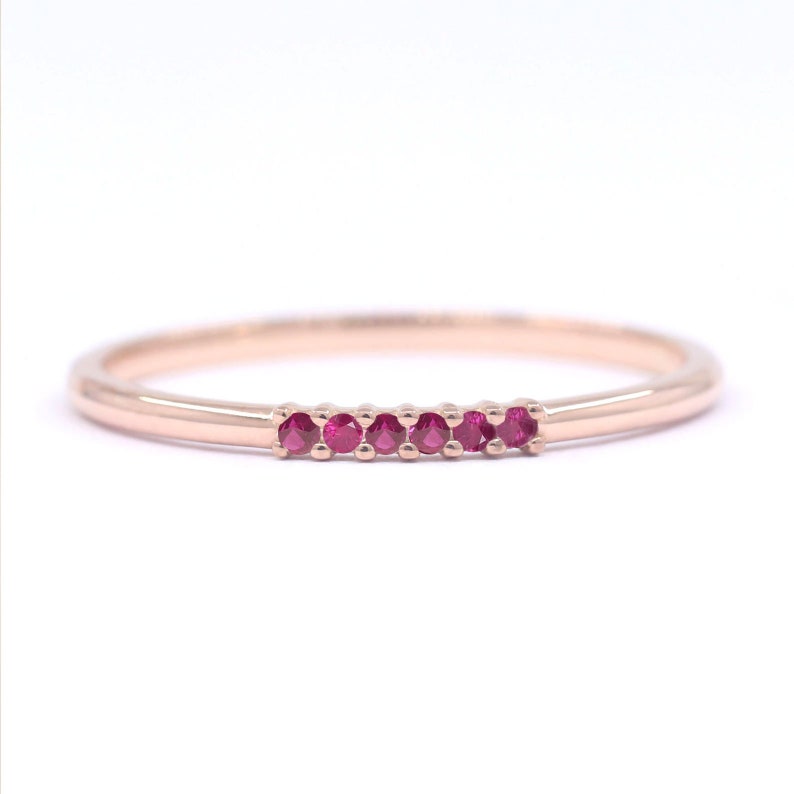Puede incluir: Un delicado anillo de banda de oro rosa con una fila de peque&ntilde;as piedras preciosas de color rosa brillante.