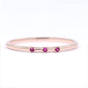 May include: A delicate rose gold band ring with three small ruby stones set in a row.
