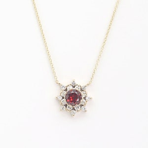 May include: A gold necklace with a red gemstone surrounded by smaller white gemstones in a flower-like design.