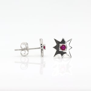 May include: A pair of silver earrings with a starburst design and a small red gemstone in the centre of each earring.
