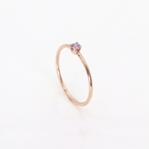May include: A delicate rose gold ring with a small, light purple gemstone set in the center.