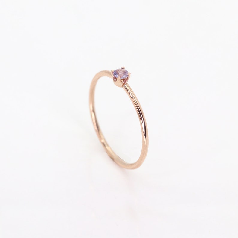 May include: A delicate rose gold ring with a small, light purple gemstone set in the center.