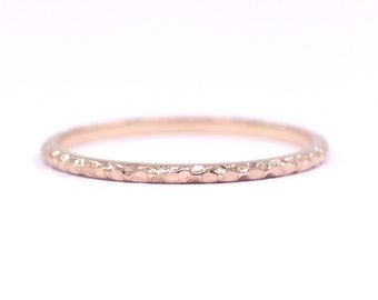 May include: A thin rose gold band ring with a hammered texture.
