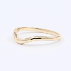 Peut inclure: Une bague dorée avec un design incurvé en forme de vague. La bague a une surface lisse et polie et un style simple et élégant. La bague est probablement en or et est conçue pour être portée au doigt.
