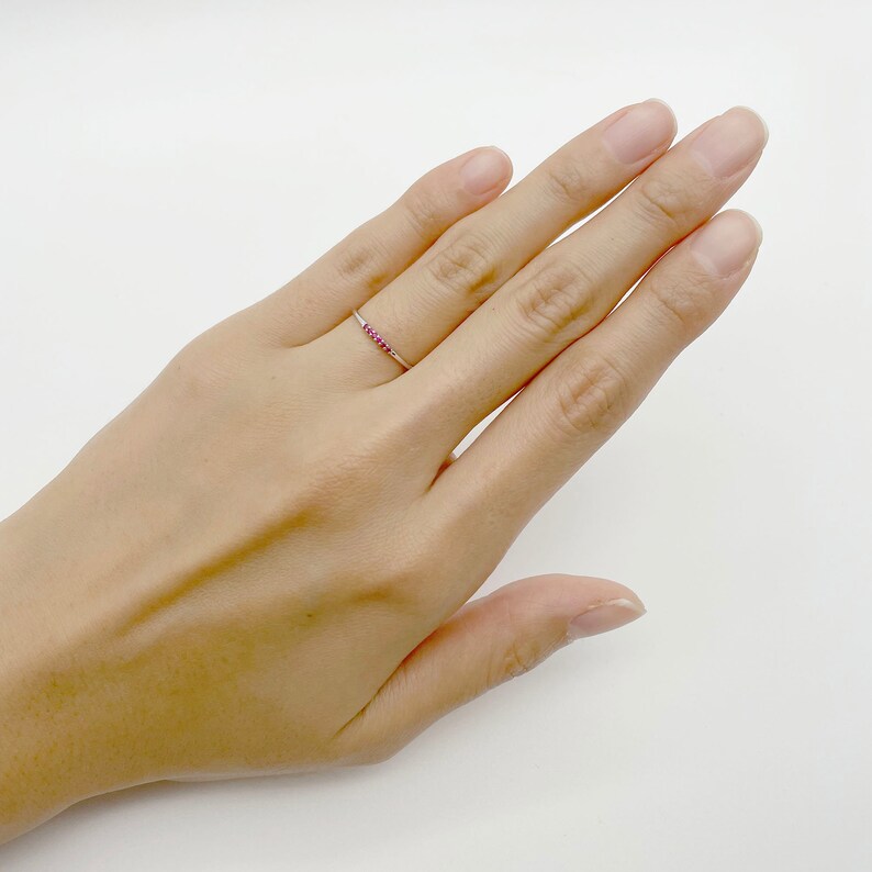 Puede incluir: Un delicado anillo de plata con una fila de peque&ntilde;as piedras preciosas rojas.