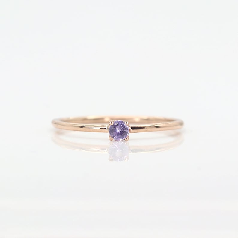 May include: A delicate rose gold band ring with a small, round, light purple gemstone.