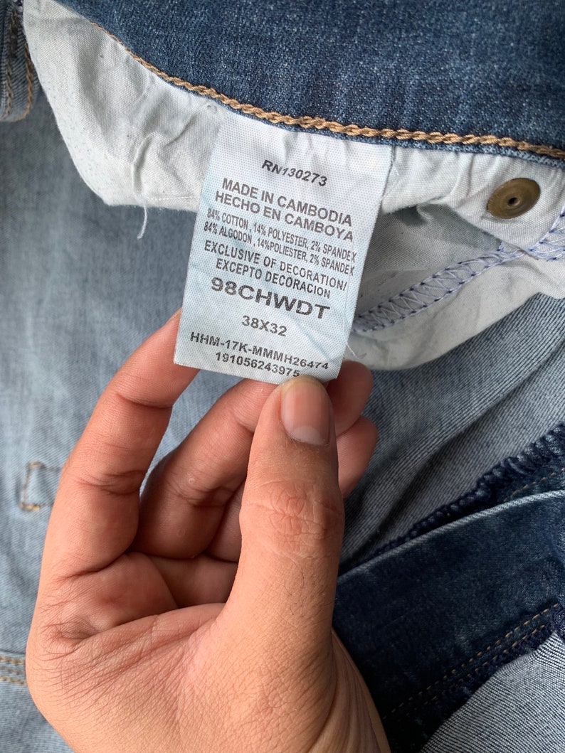 K&ouml;nnte beinhalten: Ein blaues Jeans-Etikett mit wei&szlig;em Text, der lautet: "RN130273 Made in Cambodia Hecho en Camboya 84% Cotton, 14% Polyester, 2% Spandex 84% Algodon, 14% Poli&eacute;ster, 2% Spandek Exclusive of Decoration/ Excepto Decoracion 98CHWDT 38X32 HHM-17K-MMMH26474 191056243975"
