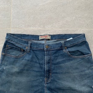 K&ouml;nnte beinhalten: Eine blaue Jeanshose mit einem braunen Leder-Wrangler-Etikett am Bund.