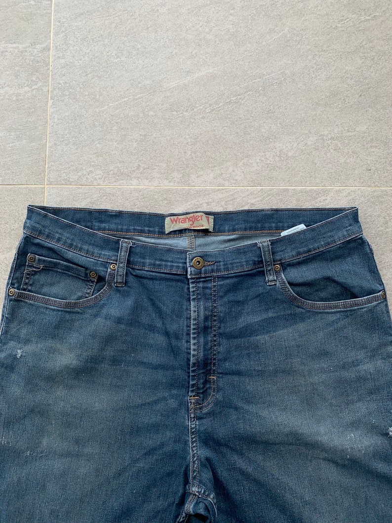 K&ouml;nnte beinhalten: Eine blaue Jeanshose mit einem braunen Leder-Wrangler-Etikett am Bund.