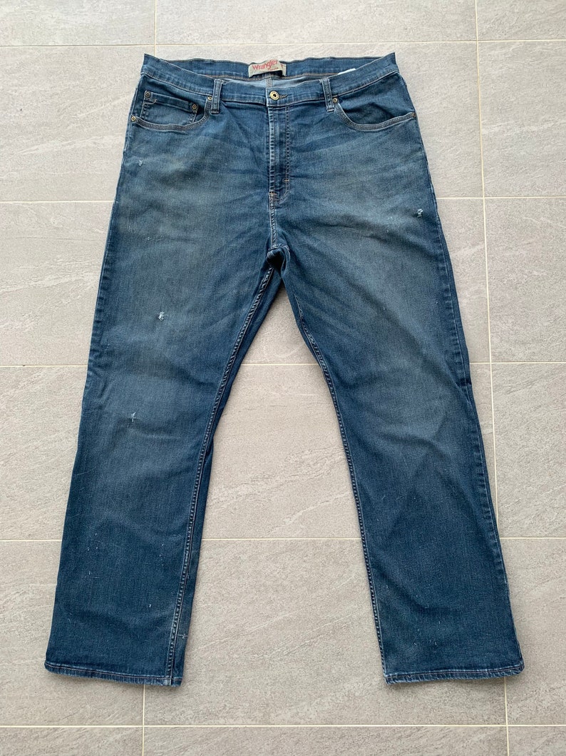 K&ouml;nnte beinhalten: Eine blaue Jeans aus Denim mit ausgewaschenem Look. Die Jeans hat einen geraden Schnitt und ein klassisches Design mit f&uuml;nf Taschen. Das Wrangler-Logo ist auf dem hinteren Bund sichtbar.