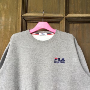 May include: Gray sweatshirt with a Fila logo embroidered on the front. The logo is in red, blue, and white and says "Fila Biella Italia".