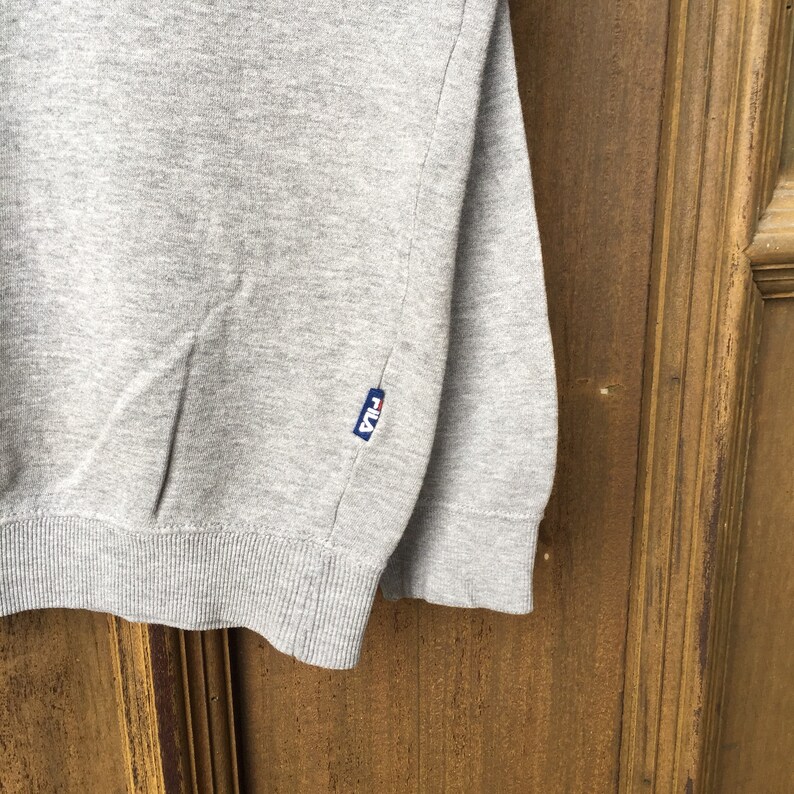 May include: Gray sweatshirt with a small blue Fila logo on the left side.