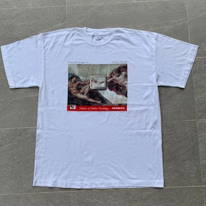 以下が含まれることがあります： ミケランジェロの「アダムの創造」の絵画をモチーフにした白いTシャツ。ただし、神の手に代わってテレビ画面が描かれている。画像の下には「Masters of Master Technology」と「HITACHI」の文字が書かれている。