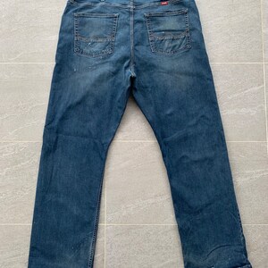 K&ouml;nnte beinhalten: Eine blaue Jeans mit ausgewaschenem Look und einem kleinen Markenetikett auf der Ges&auml;&szlig;tasche.
