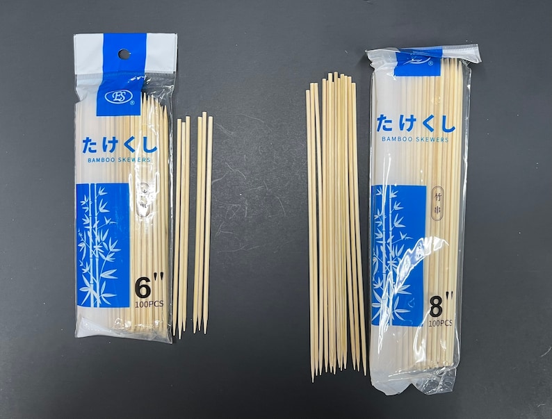 Op de afbeelding: Twee pakketten bamboesprieten, &eacute;&eacute;n pakket is 15,24 cm lang en het andere 20,32 cm lang. Beide pakketten bevatten 100 sprieten en hebben de tekst "竹串", wat in het Nederlands "bamboesprieten" betekent.
