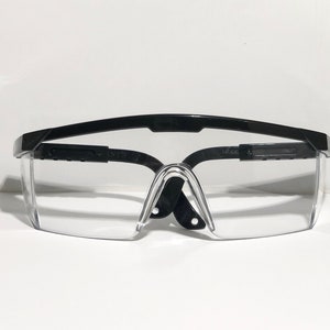 May include: Black safety glasses with clear lenses and black adjustable arms. The glasses have the words "NTS" and "MODE" printed on the arms.