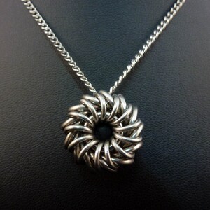 May include: A silver chain necklace with a silver pendant in the shape of a woven circle.