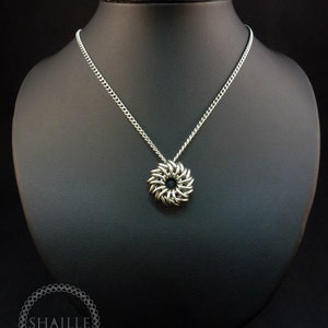 May include: A silver chainmaille necklace with a round pendant. The pendant is made of interlocking metal rings and has a slightly textured surface.