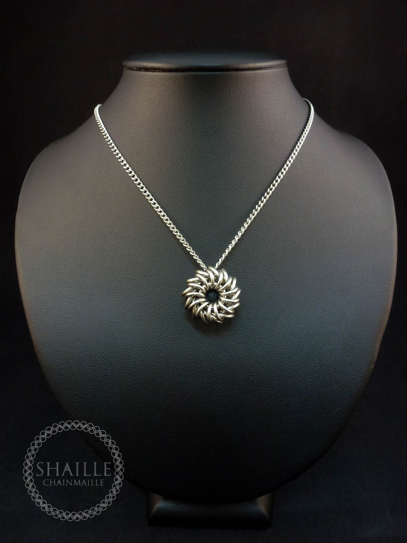 May include: A silver chainmaille necklace with a round pendant. The pendant is made of interlocking metal rings and has a slightly textured surface.