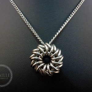 May include: A silver chainmaille necklace with a round pendant. The pendant is made of interwoven metal rings and has a circular shape.