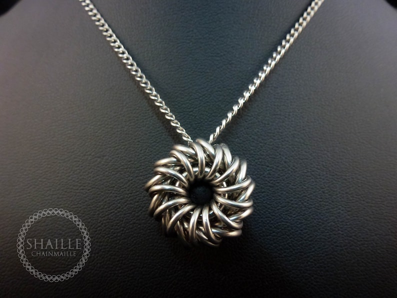 May include: A silver chainmaille necklace with a round pendant. The pendant is made of interwoven metal rings and has a circular shape.