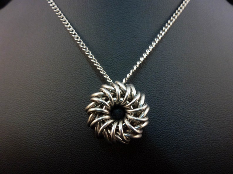 May include: A silver chain necklace with a silver pendant in the shape of a woven circle.
