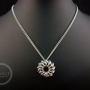 May include: A silver chain necklace with a silver chainmaille pendant in the shape of a circle. The pendant has a small hole in the center.