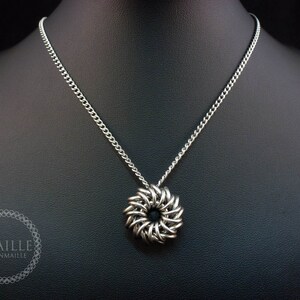 May include: A silver chain necklace with a silver chainmaille pendant in the shape of a flower. The pendant has a black center.