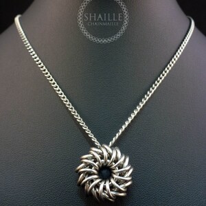 May include: A silver chain necklace with a silver chainmaille pendant in the shape of a flower. The pendant has a black center.