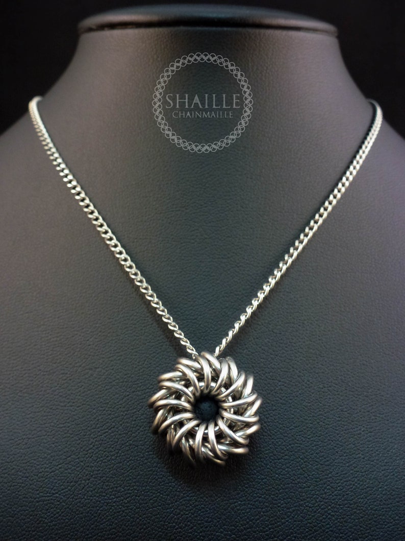 May include: A silver chain necklace with a silver chainmaille pendant in the shape of a flower. The pendant has a black center.