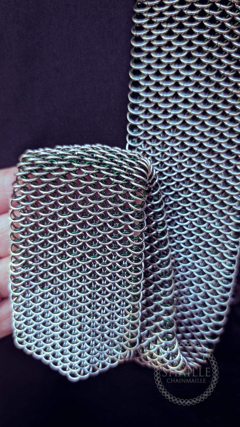 Puede incluir: Primer plano de una secci&oacute;n de cota de malla. Los eslabones met&aacute;licos est&aacute;n intrincadamente entrelazados, creando un patr&oacute;n flexible en forma de escamas. La cota de malla es de color plateado, con un ligero brillo, sobre un fondo oscuro.