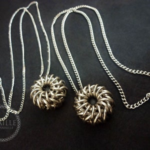 May include: Two silver chainmaille necklaces with round pendant charms. The charms are made of interwoven metal rings and have a circular hole in the center.