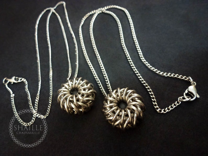 May include: Two silver chainmaille necklaces with round pendant charms. The charms are made of interwoven metal rings and have a circular hole in the center.