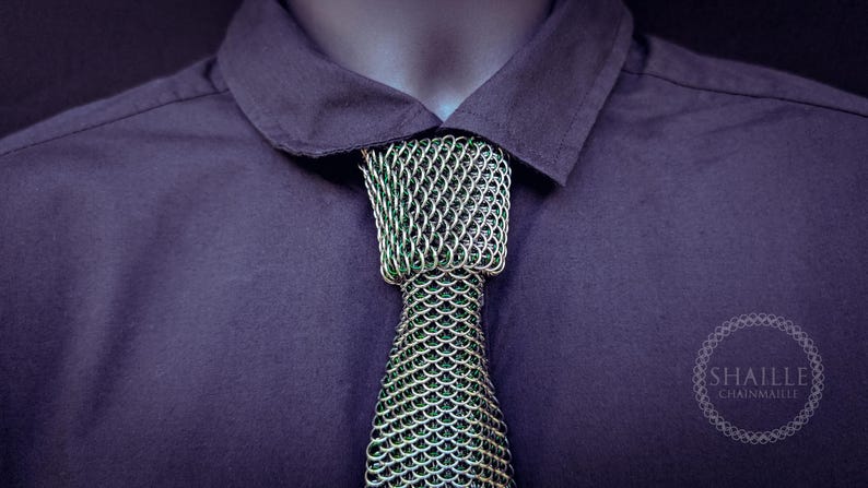Puede incluir: Primer plano de una camisa morada oscura con cuello y una corbata de cota de malla &uacute;nica. La corbata es plateada y verde, con un patr&oacute;n texturizado en forma de escamas. El logotipo "SHAILLE CHAINMAILLE" es visible.