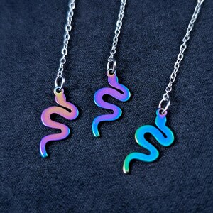 May include: Three iridescent silver chains with snake-shaped charms. The chains are hanging from a dark background.