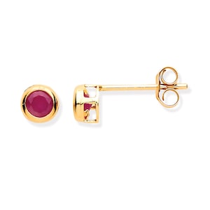 May include: A pair of gold stud earrings featuring a round, bezel-set ruby gemstone. The earrings have a post and butterfly clasp. The ruby is a deep red, and the gold setting has a polished finish.