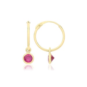 May include: Gold hoop earrings with a dangling red gemstone. The earrings have a hinged closure.