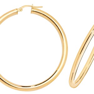 Puede incluir: Dos pendientes de aro dorados. Los pendientes son de color oro brillante y brillante. Los aros son redondos y tienen una superficie lisa y pulida. Los pendientes se muestran sobre un fondo blanco.