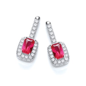 May include: A pair of silver drop earrings. Each earring has a rectangular, bright red gemstone framed by a halo of smaller, clear gemstones. The top section of each earring is a straight bar set with clear gemstones.