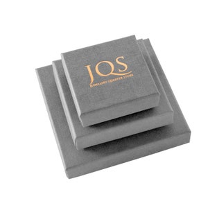 Puede incluir: Tres cajas de joyer&iacute;a grises de diferentes tama&ntilde;os est&aacute;n apiladas. La caja superior tiene el texto dorado "JQS JEWELLERY QUARTER STORE" impreso en la tapa. Las cajas est&aacute;n hechas de un material texturizado.
