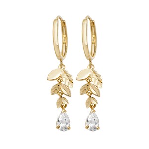 May include: Gold hoop earrings with a dangling cluster of leaf charms and a pear-shaped clear stone.
