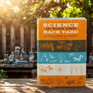 May include: A vintage book titled "SCIENCE IN YOUR OWN BACK YARD" by Elizabeth K. Cooper. The book has an orange, green, and blue cover with illustrations of plants, insects, and animals. The book is on a wooden surface.