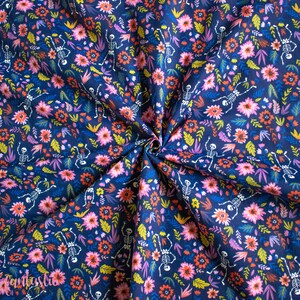 May include: A dark blue fabric with a repeating pattern of skeletons dancing among pink, orange, and yellow flowers. The fabric is folded in a spiral.