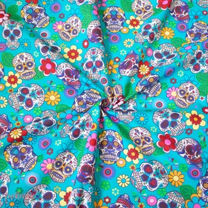 Op de afbeelding: Een turquoise stof met een herhalend patroon van kleurrijke suiker schedels en bloemen. De schedels zijn versierd met ingewikkelde details en hebben een eigenzinnige, feestelijke uitstraling.