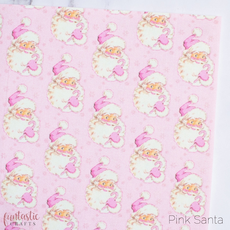 May include: Pink and white patterned fabric featuring a repeating design of Santa Claus holding a candy cane. The background is a light pink with a subtle snowflake pattern.