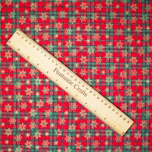 K&ouml;nnte beinhalten: Roter und gr&uuml;ner karierter Stoff mit einem goldenen Schneeflockenmuster. Ein Holzliniall mit der Aufschrift "Fantastic Crafts" liegt auf dem Stoff.